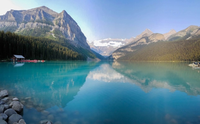 A red boathouse is nestled on the shores of Lake Louise, a vibrant blue glacial lake located in Banff National Park