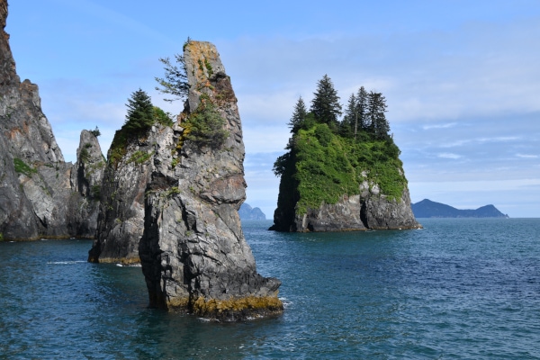 Cove of Spires rises from the blue water of Resurrection Bay in Kenai Fjords National Park with mountains in the distance