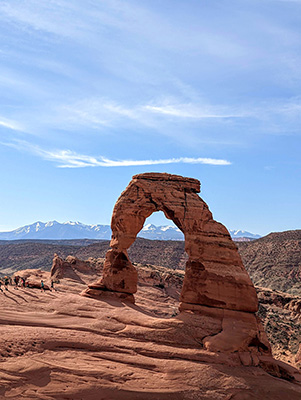 A large red rock arch with snow capped mountains behind it