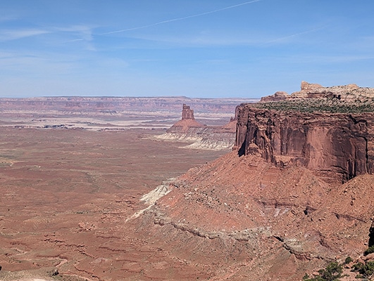 A distant red rock formation juts up from the red desert  floor, past a closer red rock cliff face on the right