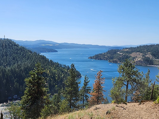 The dark blue water of Lake Coeur d'Alene is seen from a hill with other hills surrounding it