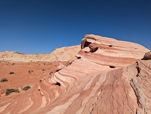 A large red rock with lighter stripes rises from the red desert floor