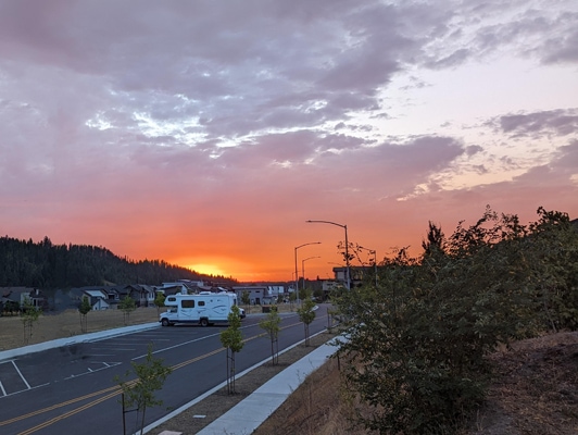 An orange sun sets behind some purple clouds with a road and RV in the foreground