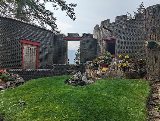 The grass courtyard of a house made of square glass bottles frames a distant view of the mountains