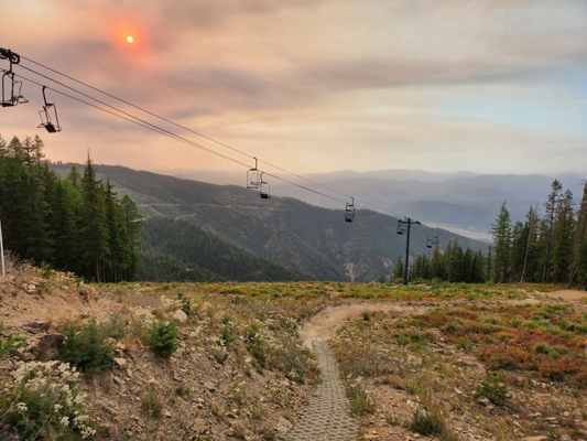 An orange sun burns through smoky skies over mountains and a ski lift