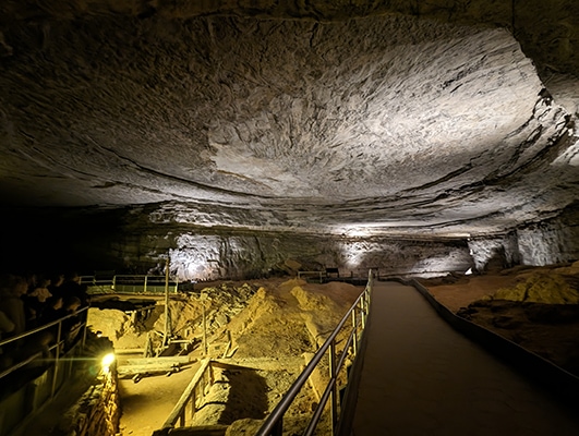 A large cave with lighting and a small mining operation sunken in the floor
