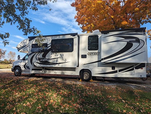 A large white motorhome parked under a tree with orange leaves