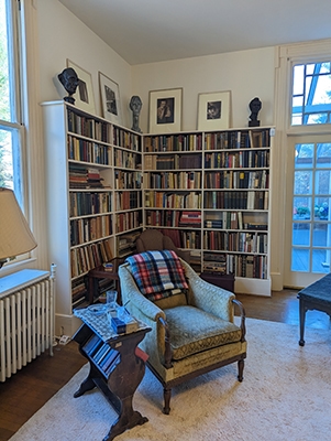 An armchair in a corner of a room with full bookshelves filling the corner behind it