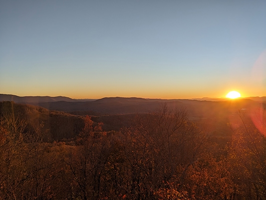 The orange sun is sinking behind mountains, giving them a golden glow