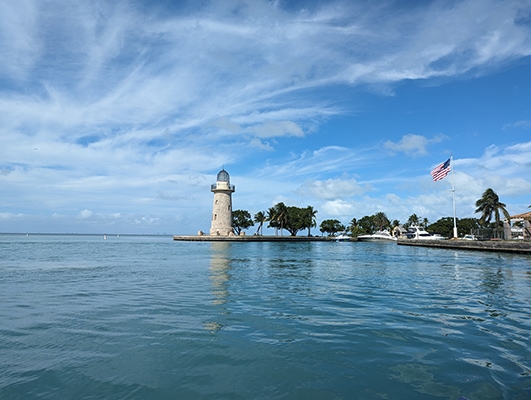 A stone lighthouse on an island's point with blue sea and blue sky surrounding it