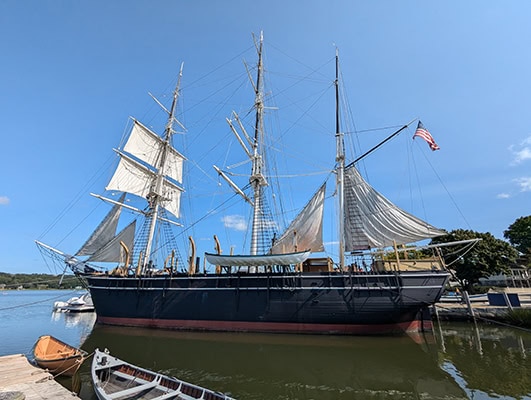 An ol 3-masted sailing ship floats on the water on a cloudless day