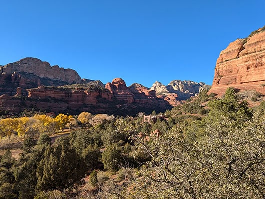 A red rock canyon disappears around a curve and autumn trees fill in the mouth of the canyon