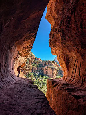 Looking out of a red rock cave to more red rock formations and greenery in the distance