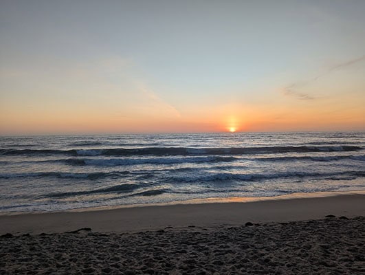 The orange sun sinks into the dark blue ocean