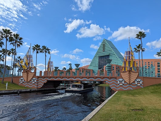A brown bridge crosses a small channel. Either side of the bridge is designed to look like a ship coming toward the viewer. A small boat is passing under the bridge